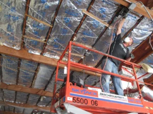 A worker installs foil-faced attic insulation between roof rafters from a lift during a Ferndale church remodel.