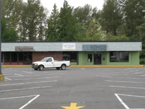 A low storefront with a children's consignment sign faces an empty parking lot, with a white pickup parked outside.