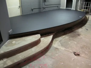 A curved stage platform with a finished dark top and unfinished steps during church remodeling in Ferndale.