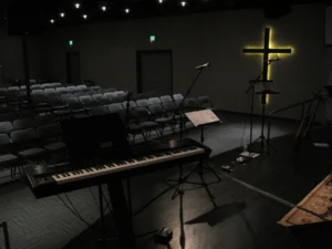 Empty sanctuary with a keyboard, microphones, rows of chairs, and a glowing cross at a Ferndale church build.